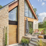 La porte d'entrée en bois et aluminium DRYADE dans sa finition bois naturel sur une façade de maison contemporaine.