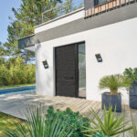 La porte d'entrée en bois et aluminium DRYADE dans sa finition bois brûlé sur une façade de maison contemporaine